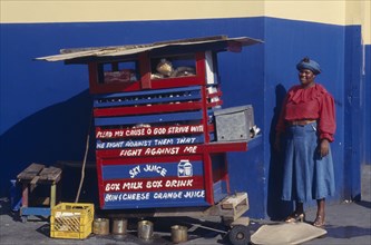 WEST INDIES, Jamaica, Kingston, Street vendor with religious text painted on stall.