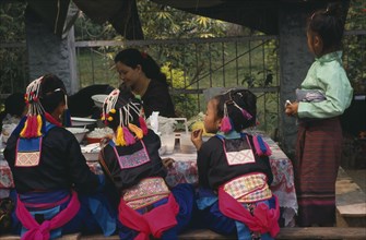 LAOS, Luang Prabang, Hmong girls in traditional dress eating at roadside foodstall.