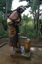 TANZANIA, West, Great Lakes Region, Woman with baby tied on her back collecting water from pump in