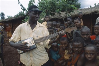 TANZANIA, West, Great Lakes Region, Refugee children listening to boy playing guitar made from
