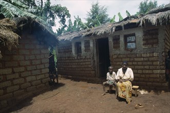 TANZANIA, West, Great Lakes Region, "Refugee woman and child sitting outside thatched, mud brick