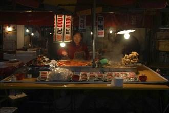 KOREA, Seoul, Namdaemun Market on a cold December night with a woman working at a street restaurant