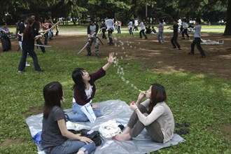 JAPAN, Honshu, Tokyo, "Harajuku. Yoyogi Park. Miki Tomiyoka, aged 23, blows bubbles for two friends
