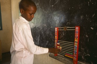 SOMALILAND, Hargeisa, Boy using an abacus in school classroom with blackboard on wall behind.