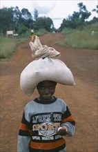 TANZANIA, West, Great Lakes Region, Young refugee girl carrying sack of food on her head with