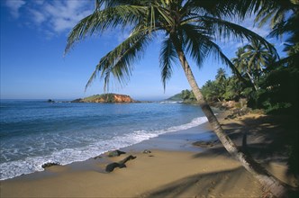 SRI LANKA, Mirissa, View along sandy beach with overhanging palms and distant rocky outcrop