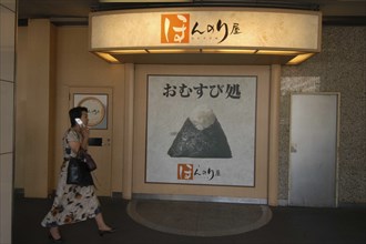 JAPAN, Honshu, Tokyo, Onigiri rice ball shop sign in front of Tokyo Station with passing woman
