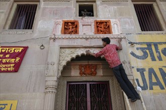 INDIA, Uttar Pradesh, Varanasi , Deep Diwali Festival with young man decorating a doorway