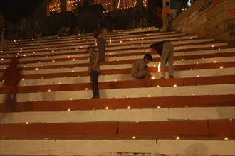 INDIA, Uttar Pradesh, Varanasi, Deep Diwali Festival with young boys lighting oil lamps on steps