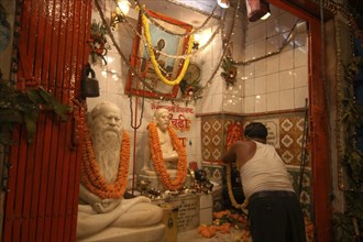 INDIA, Uttar Pradesh, Varanasi, Dasaswamedh Ghat with a man cleaning a shrine to a Hindu Saint