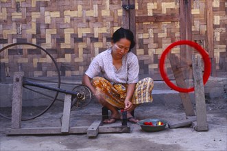 MYANMAR, Kachin State, Myitkyina, Jinghpaw woman spinning thread onto a bobbin for weaving at a