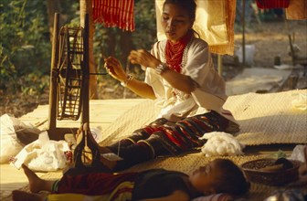 THAILAND, Chiang Mai Province, Lawa woman spinning thread inside her house with her young son lying