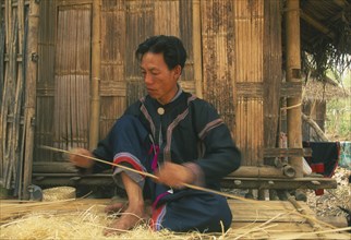 THAILAND, Chiang Mai Province, Red Lahu man shaving bamboo into strips