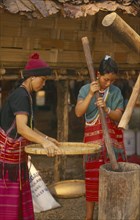 THAILAND, Chiang Mai, Sgaw Karen woman pounding rice by hand while another sifts with a large