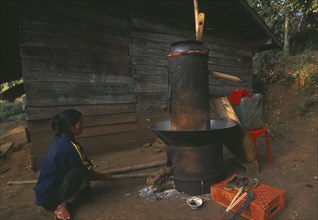 THAILAND, Chiang Rai Province, Doi Lan, Lisu woman stoking fire of her still for making corn