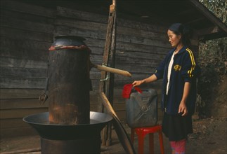THAILAND, Chiang Rai Province, Doi Lan, Lisu woman checking cloth filter on the spout of her still