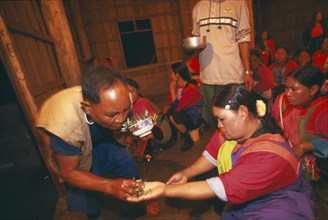 THAILAND, Chiang Rai Province, Doi Lan, Lisu shaman spraying supplicants hand at healing ceremony