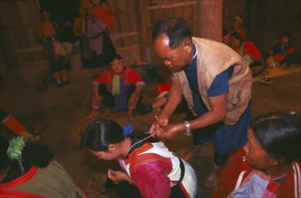 THAILAND, Chiang Rai Province, Doi Lan, Lisu shaman tying string around supplicants neck at healing