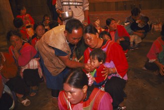 THAILAND, Chiang Rai Province, Doi Lan, Lisu shaman giving infant liquid at healing ceremony