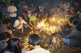THAILAND, Chiang Mai, Wat Jedi Luang, Inthakhin Ceremony. People lighting candles on offerings