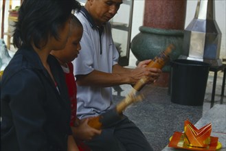 THAILAND, Chiang Mai, Wat Chai Mong Kon, Man with son kneeling before an altar shaking containers
