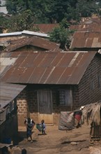 UGANDA, Kampala, Kamwoyke slum area.  Woman and child outside brick hut with corrugated iron roof.
