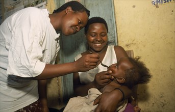 UGANDA, General, Young child held by mother receiving medicine on spoon.