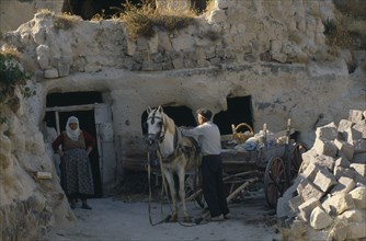 TURKEY, Cappadocia, Uchisar, Couple harnessing pony to wooden cart.  Inhabitants of cave dwellings