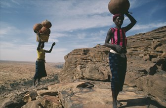 MALI, Bandiagara Cliffs, One woman carrying beer and another pots on their heads standing at the