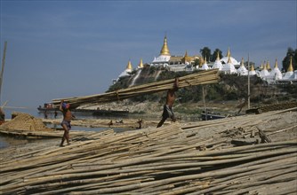 MYANMAR, Mandalay, Unloading lengths of cane on the banks of the Ayeyarawady overlooked by temple