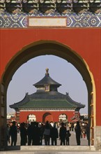 CHINA, Beijing, Temple of Heaven.  Temple and tourists framed by red painted archway.