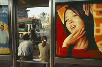 CHINA, Beijing, People waiting at bus stop south of Tiananmen Square with advertising hoarding