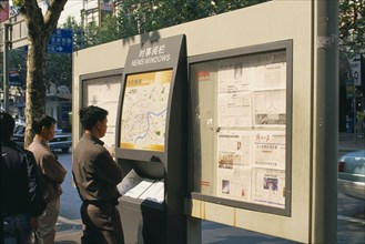 CHINA, Shanghai, Nanjing Road.  Men reading map and newspapers displayed on boards in ‘news