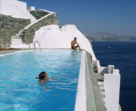 GREECE, Cyclades Islands, Santorini, Imerovigli.  Couple in swimming pool overlooking sea.