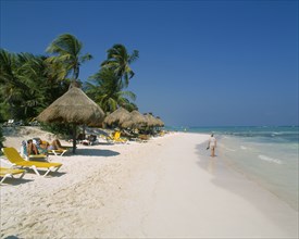 MEXICO, Quintana Roo, Tulum, Stretch of sandy beach with people on sun loungers under a line of