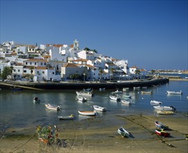 PORTUGAL, Algarve, Ferragudo, White painted town buildings overlooking harbour and moored boats.