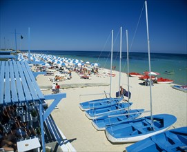 TUNISIA, Port el Kantaoui, Busy sandy beach with tourist boats and pedelos for hire and lines of