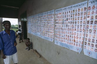 LIBERIA   , Margibi, Kakata, Man standing next to Red Cross tracing posters of Liberian children