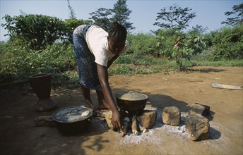 LIBERIA   , Nimba, Saclepea, Young woman cooking on open wood fire.