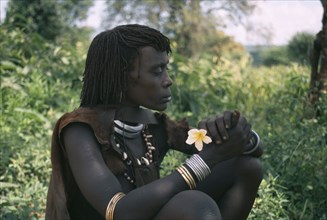 ETHIOPIA, Demeka, Portrait of Hamer woman holding frangipani flower.
