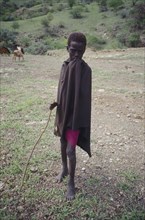 TANZANIA, Tribal People, Portrait of young Masai boy with goats grazing in the background.