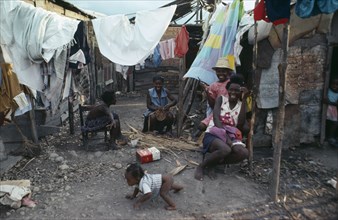 HAITI, People, Group of laughing women and children in shanty village sitting outside underneath