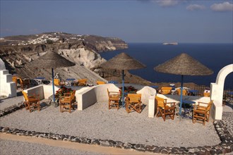 GREECE, Cyclades, Santorini, Terrace with tables and chairs under thatch umbrellas overlooking