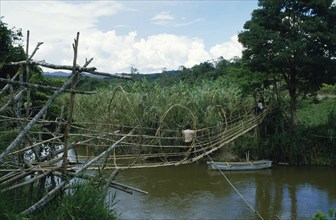 INDONESIA, Sulawesi, Napu Valley. Bamboo bridge over river with people crossing over.