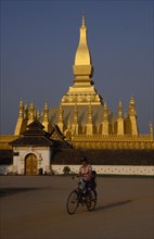 LAOS, Vientiane, Pha That Luang temple exterior with cyclist in foreground.