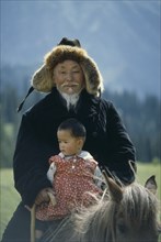 CHINA, Xinjiang, Kazakh grandfather and granddaughter on horse.