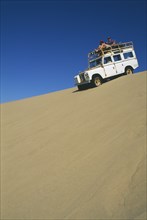 NAMIBIA, Skeleton Coast, Terrace Bay, Dune driving on the Roaring Dunes with jeep on crest of dune.