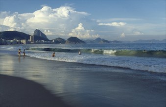 BRAZIL, Rio de Janeiro, Beach with people playing in the surf.  City buildings and Sugar Loaf