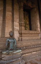 LAOS, Vientiane, Haw Pha Kaew temple.  Seated Buddha statue in front of carved wall.