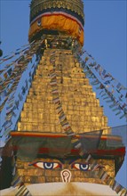 NEPAL, Kathmandu, Bodnath Stupa, Detail of spire of stupa with painted eyes and hung with prayer